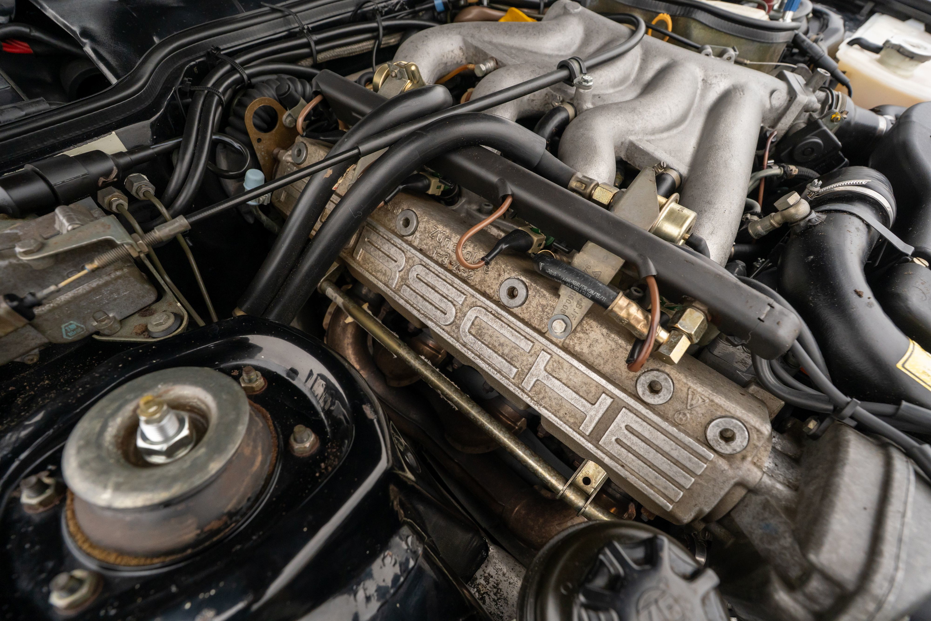 Closeup of a 1986 Porsche 944 Turbo engine bay, showing the PORSCHE embossed valve cover.