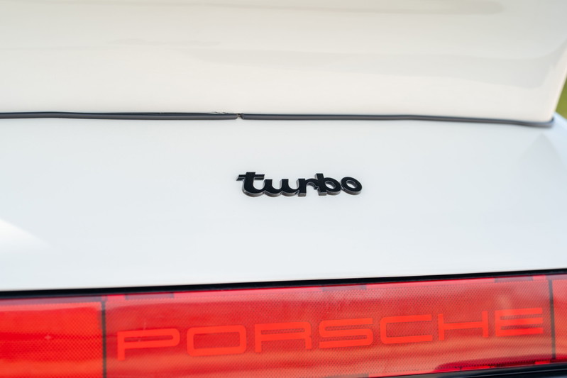 Close-up of a white 1988 Porsche 930 Turbo slantnose rear badge.