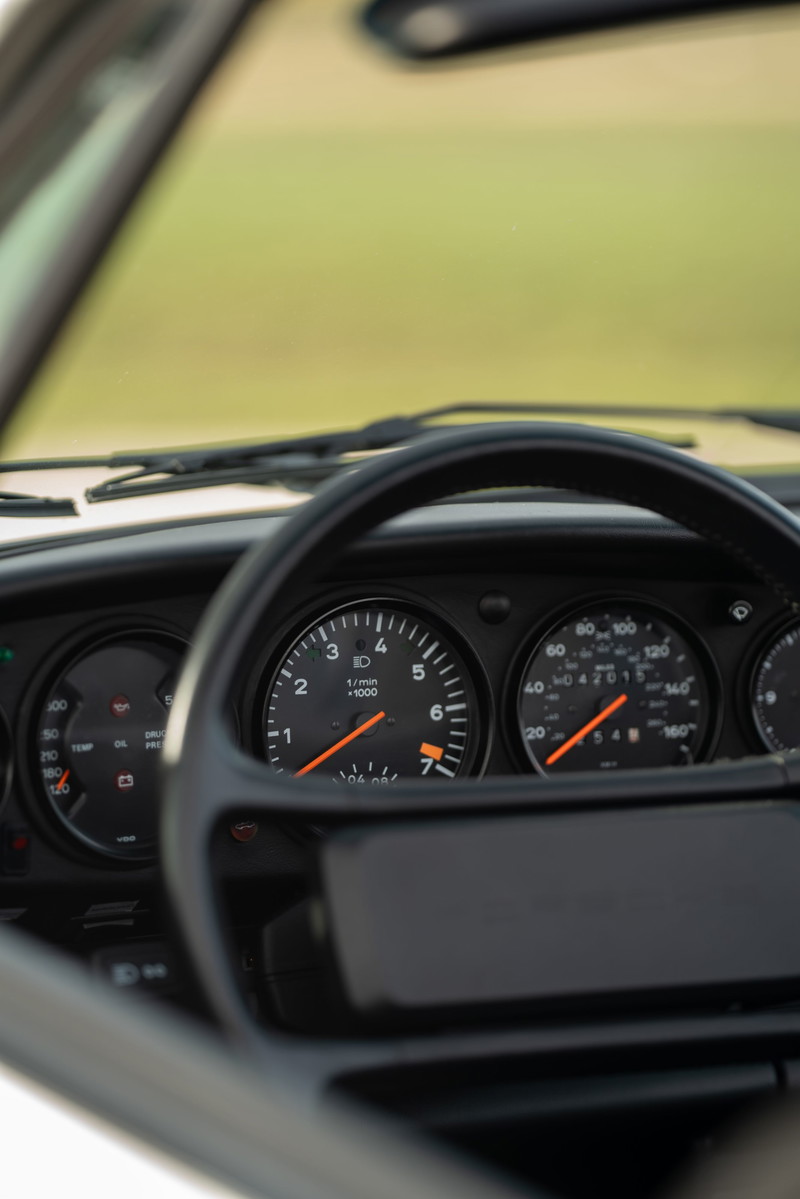 Interior of a white 1988 Porsche 930 Turbo Slantnose, showing the instrument cluster with tachometer.