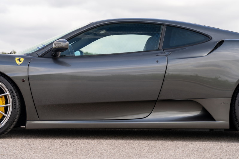 Close-up of a Grigio Silverstone 2007 Ferrari F430's side profile, showing yellow brake calipers behind silver rims.