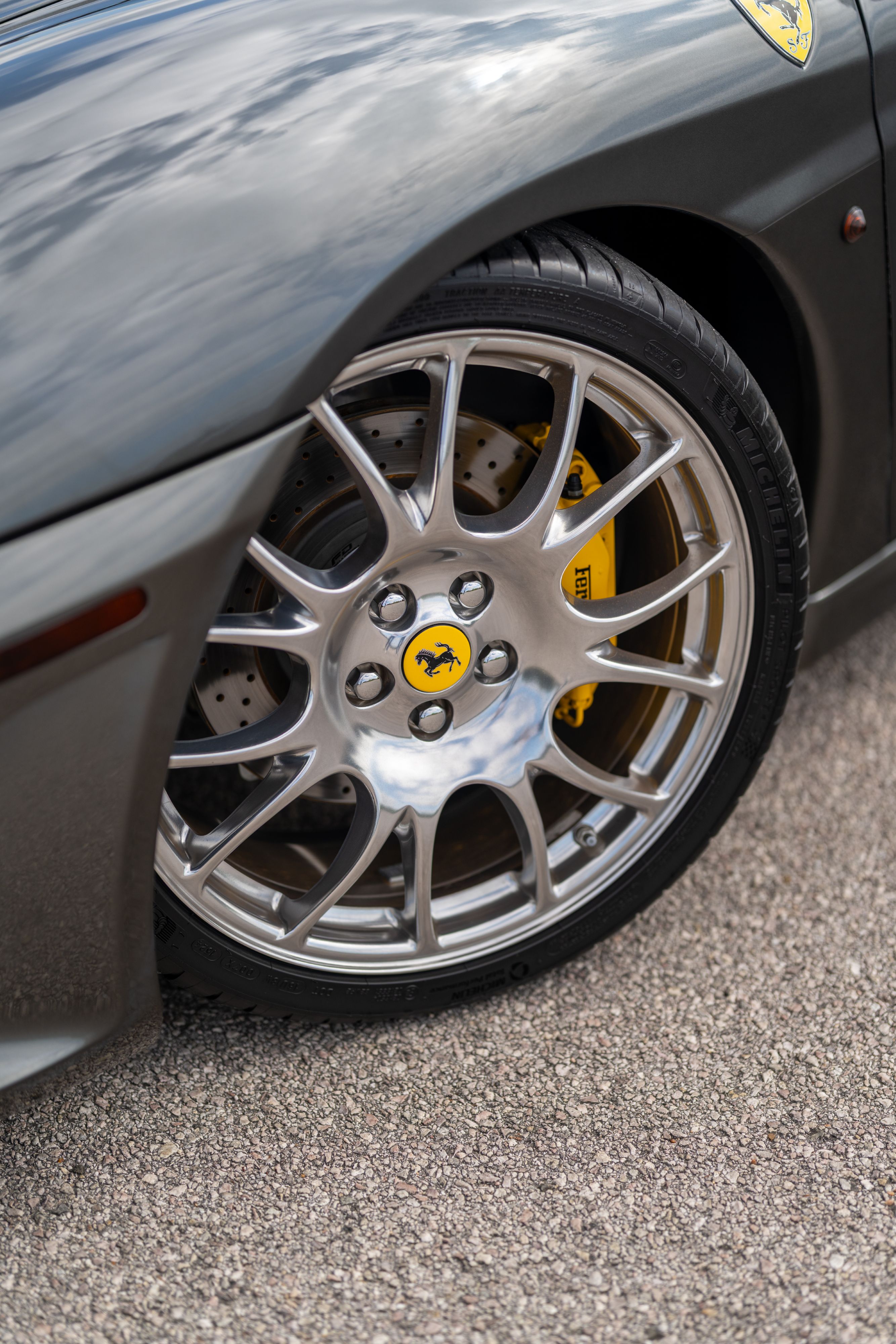 Close-up of a Grigio Silverstone Ferrari F430 front wheel with yellow brake calipers and a Cavallino Rampante center cap.