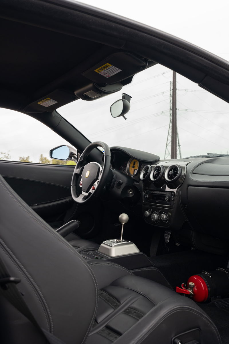 Interior view of a Grigio Silverstone 2007 Ferrari F430 6-speed with black leather seats and silver gated shifter.