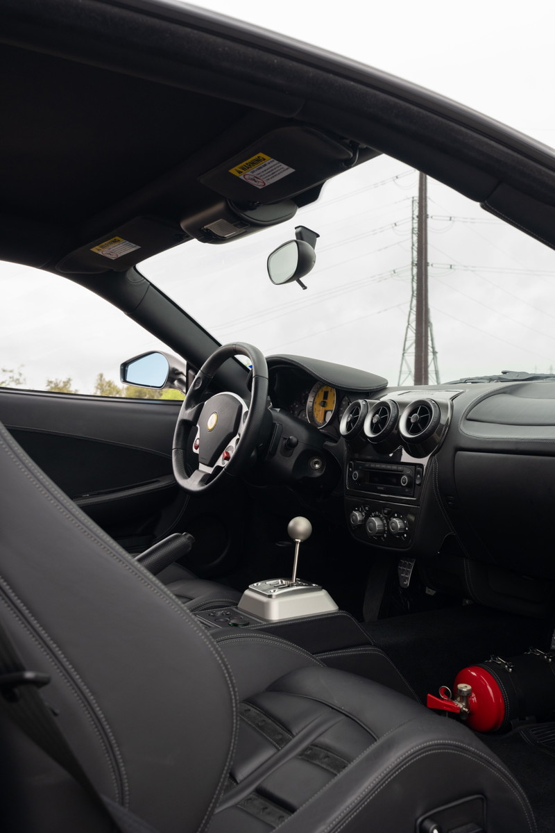 Interior view of a Grigio Silverstone 2007 Ferrari F430 6-speed with black leather seats and silver gated shifter.