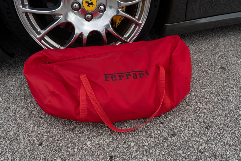 Red Ferrari branded car cover by a silver rim with yellow brake caliper.
