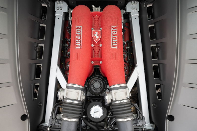 Close-up of the twin red Ferrari intake manifolds and engine bay of a Grigio Silverstone 2007 Ferrari F430.