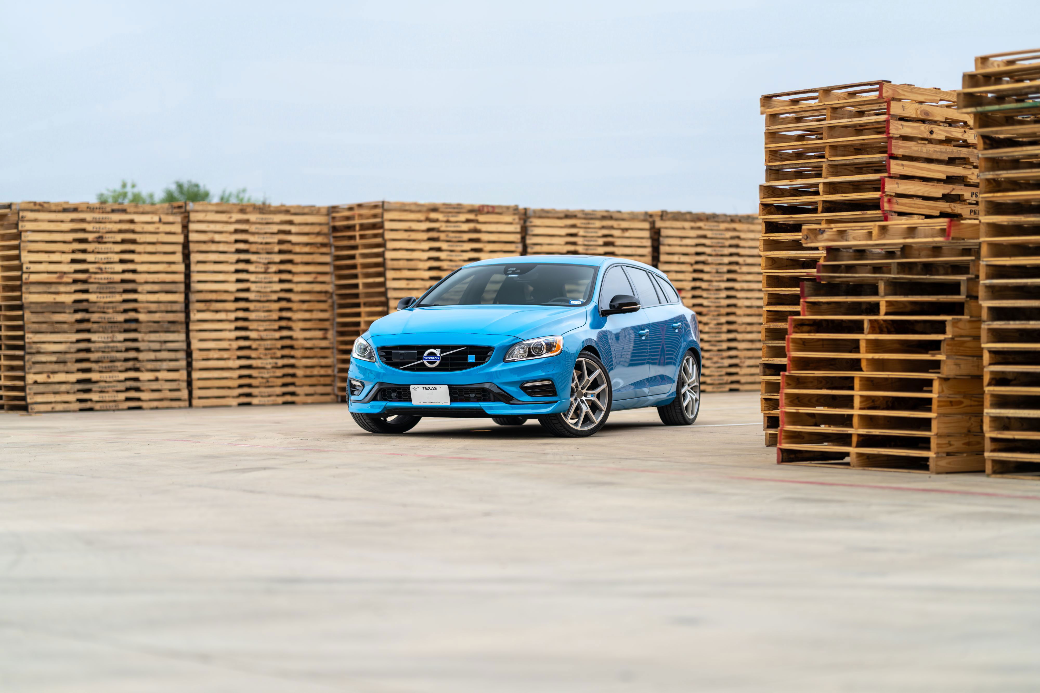 A rebel blue 2015 Volvo V60 Polestar with silver rims parked in front of wood pallets.