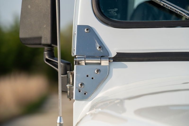 Close-up of a white 1983 Jeep Scrambler door hinge and side mirror mount.