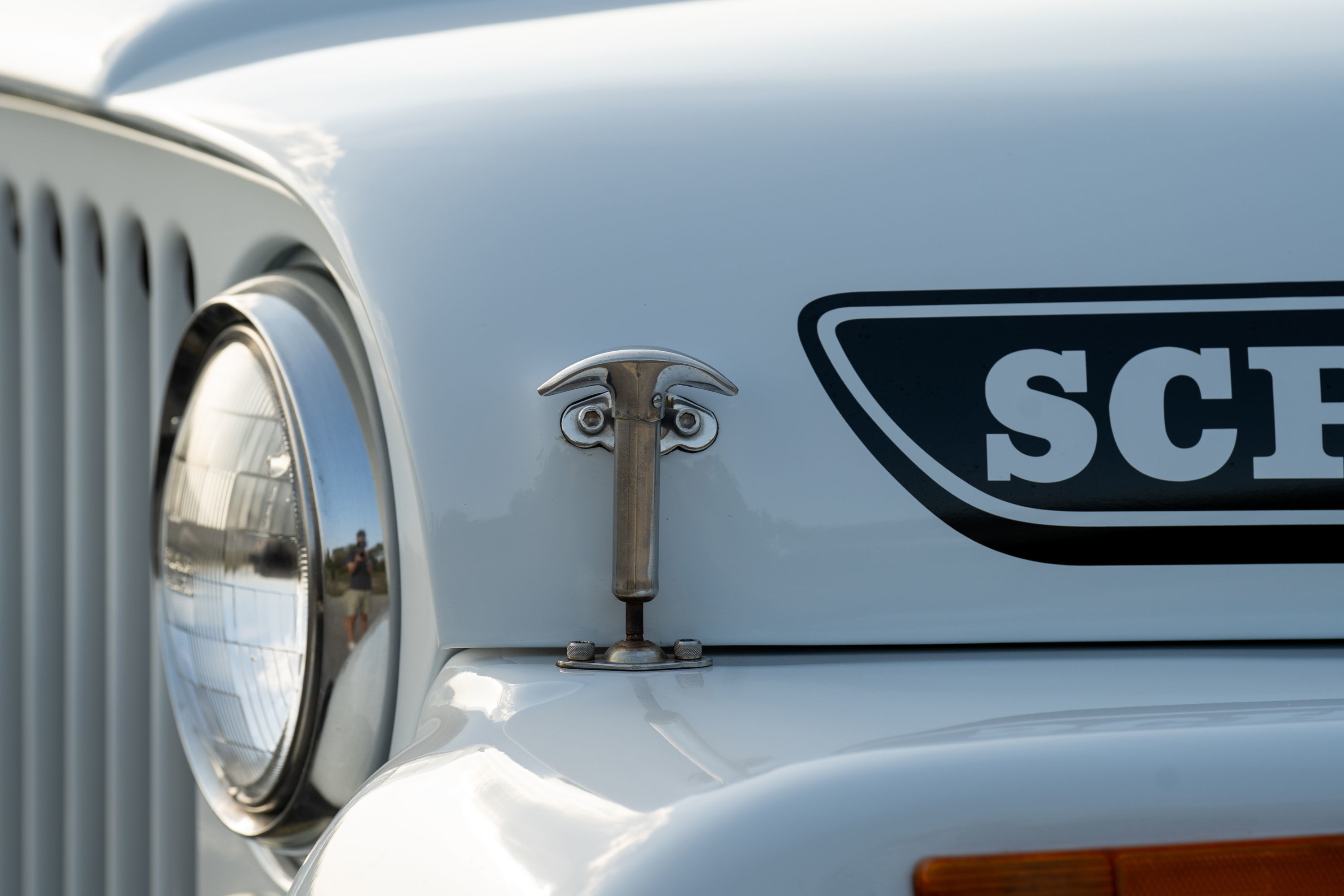 White 1983 Jeep Scrambler with a chrome hood latch and Scrambler badge.