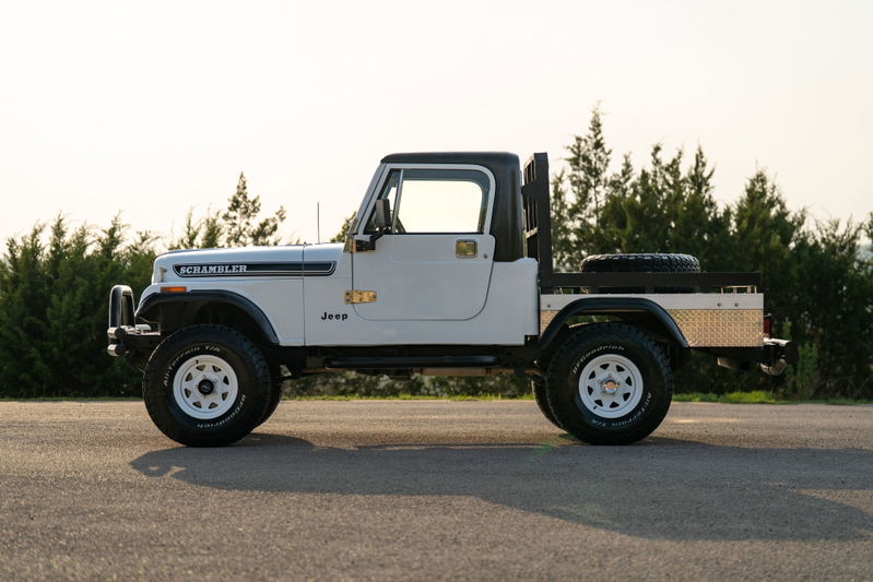 White 1983 Jeep CJ-8 Scrambler with flatbed, white rims, and black trim.