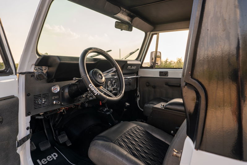 1983 white Jeep Scrambler CJ-8 interior, featuring a Jeep-branded steering wheel and diamond-stitched seats.