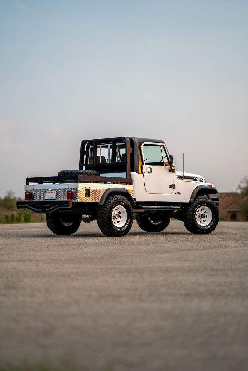 White 1983 Jeep CJ8 Scrambler with a flatbed conversion, roll cage, and white rims.