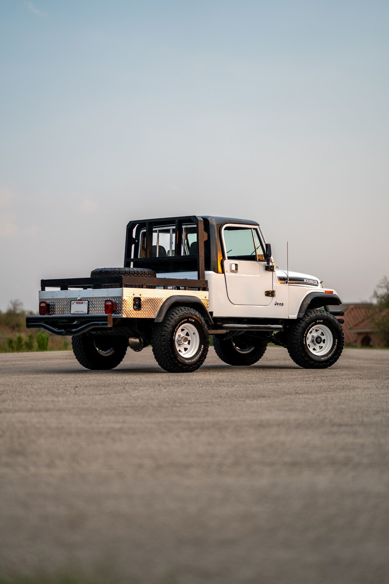 White 1983 Jeep CJ8 Scrambler with a flatbed conversion, roll cage, and white rims.