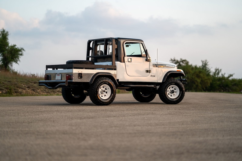 White 1983 Jeep Scrambler CJ-8 with custom flatbed, diamond plate trim, and white rims.