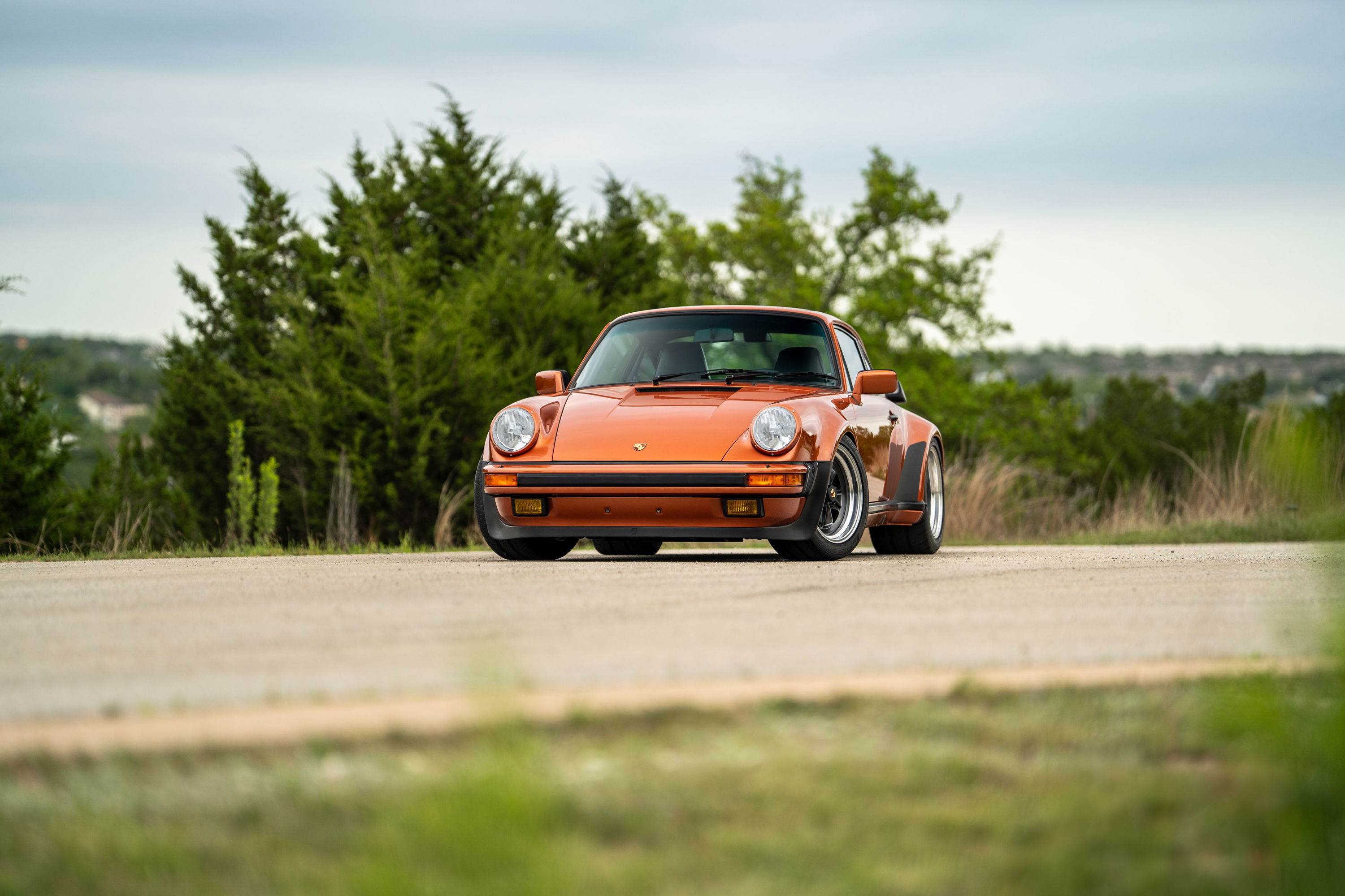 Orange 1986 Porsche 930 Turbo with black trim and rims, viewed from the front ¾ angle on a road.