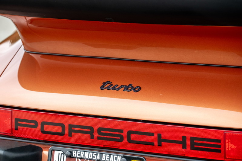 Close-up of an orange metallic 1986 Porsche 930 Turbo rear badging.