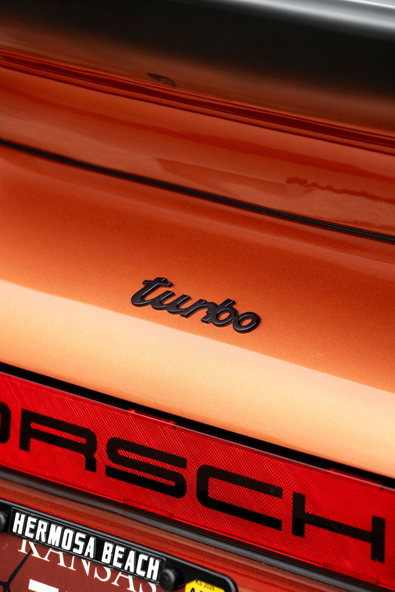 Close-up of an orange metallic 1986 Porsche 930 Turbo rear emblem and trim.