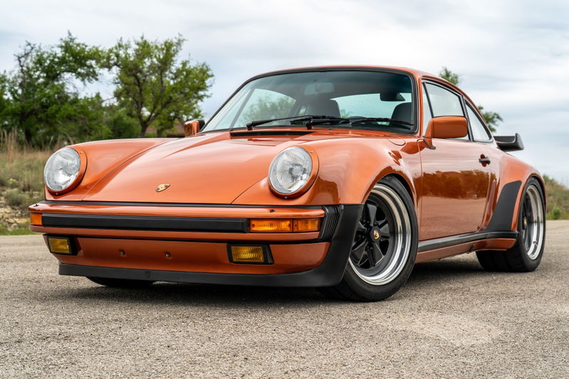 Front 3/4 view of an orange metallic 1986 Porsche 930 Turbo with black trim and Fuchs rims.