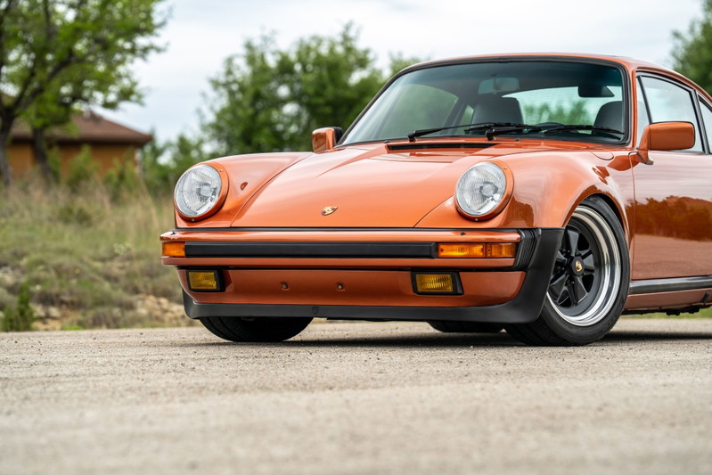 1986 Porsche 930 Turbo in orange metallic, featuring black Fuchs rims.
