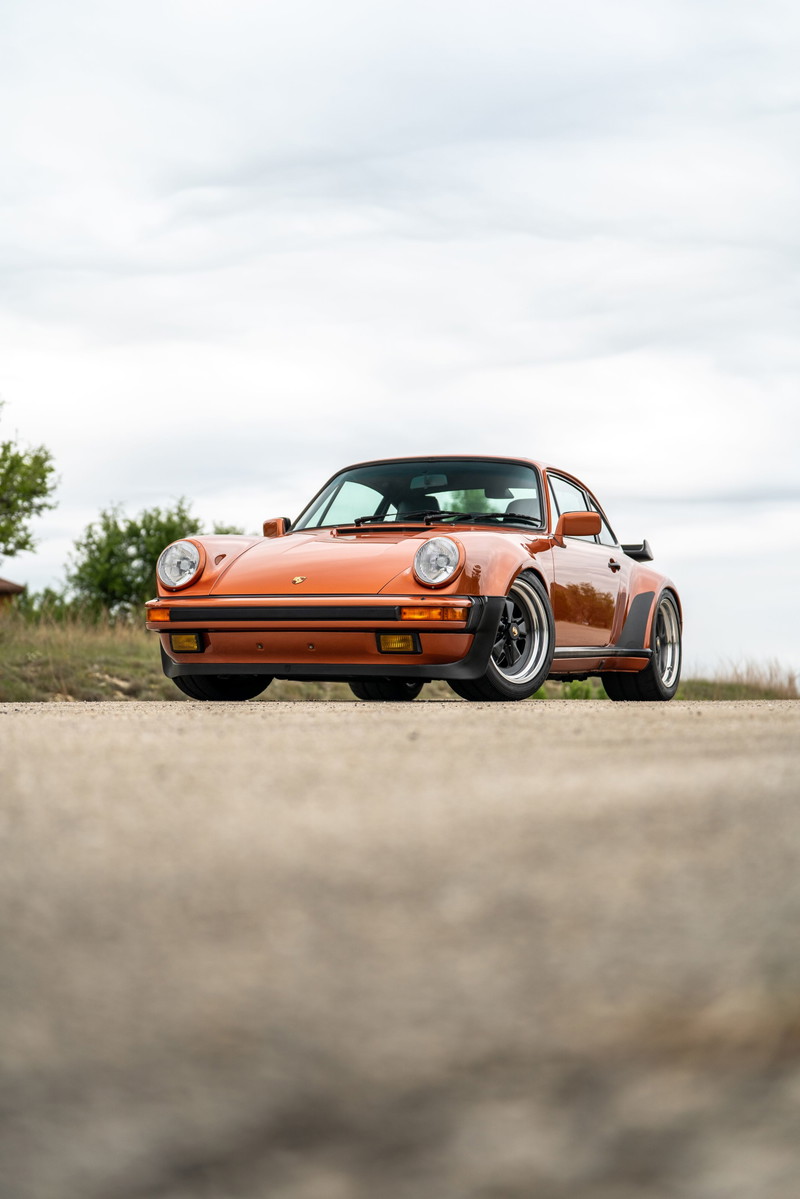Front view of an orange metallic 1986 Porsche 930 Turbo with black trim and Fuchs rims.