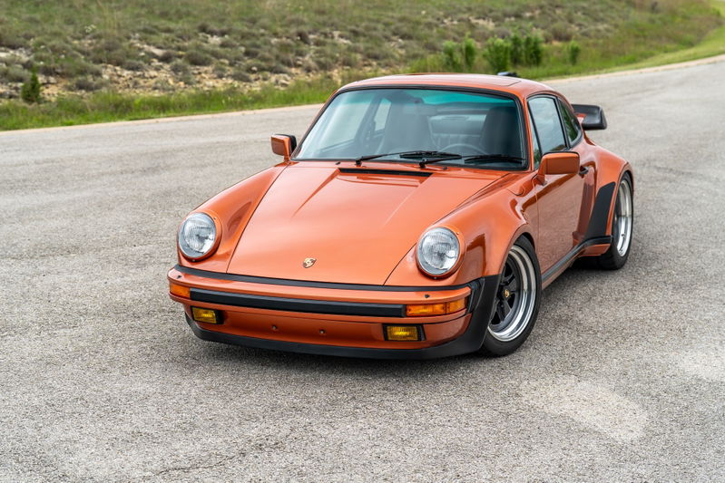1986 Porsche 930 Turbo in metallic orange, with Fuchs wheels and wide body trim.