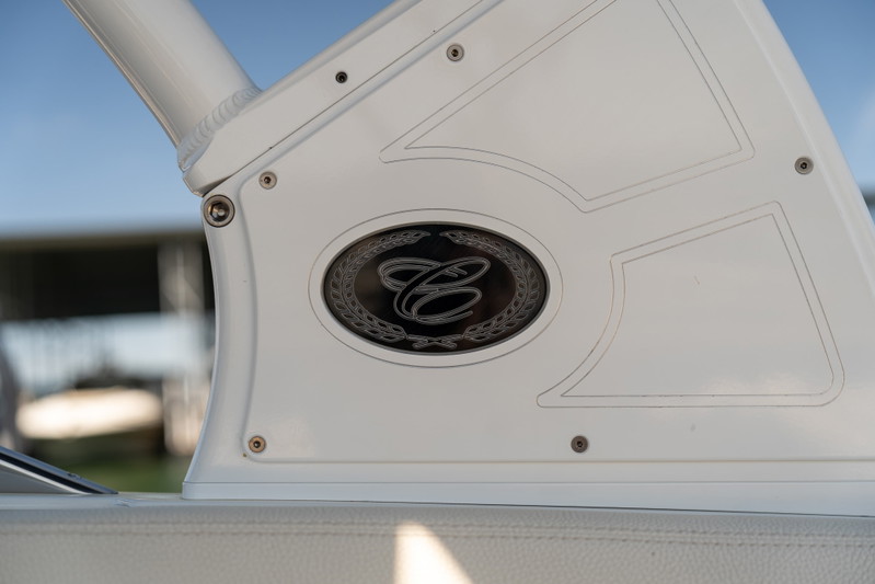 Close-up of a Cobalt R7 Surf boat's white trim featuring an oval emblem with a stylized 'C' logo and laurel wreath.
