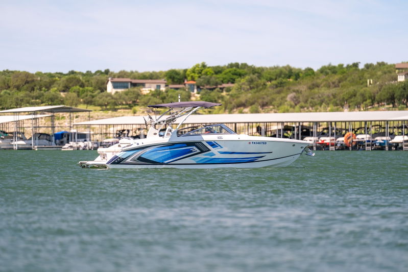A white Cobalt R7 Surf boat with blue racing livery cruises on a lake.