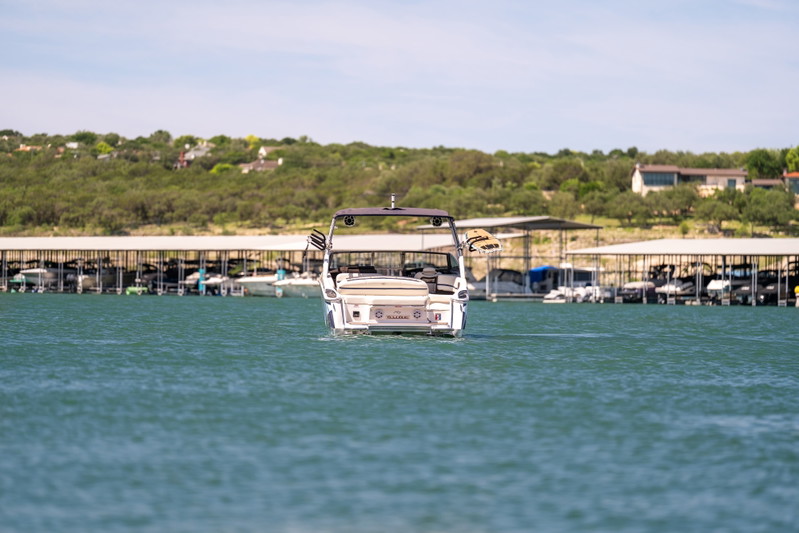 Rear view of a white Cobalt R7 Surf boat, on a lake, with boat docks in the background.