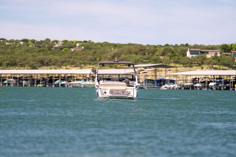 Rear view of a white Cobalt R7 Surf boat, on a lake, with boat docks in the background.
