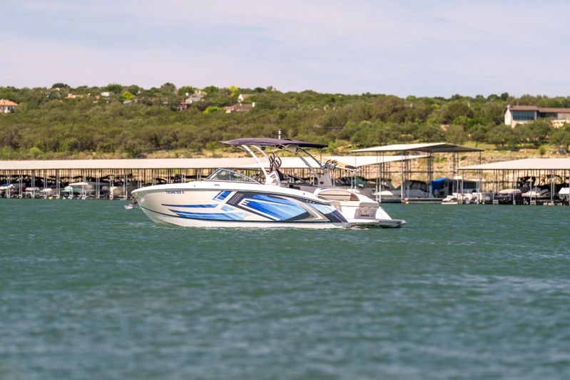 2018 Cobalt R7 Surf boat with blue and silver livery in the water near a marina.