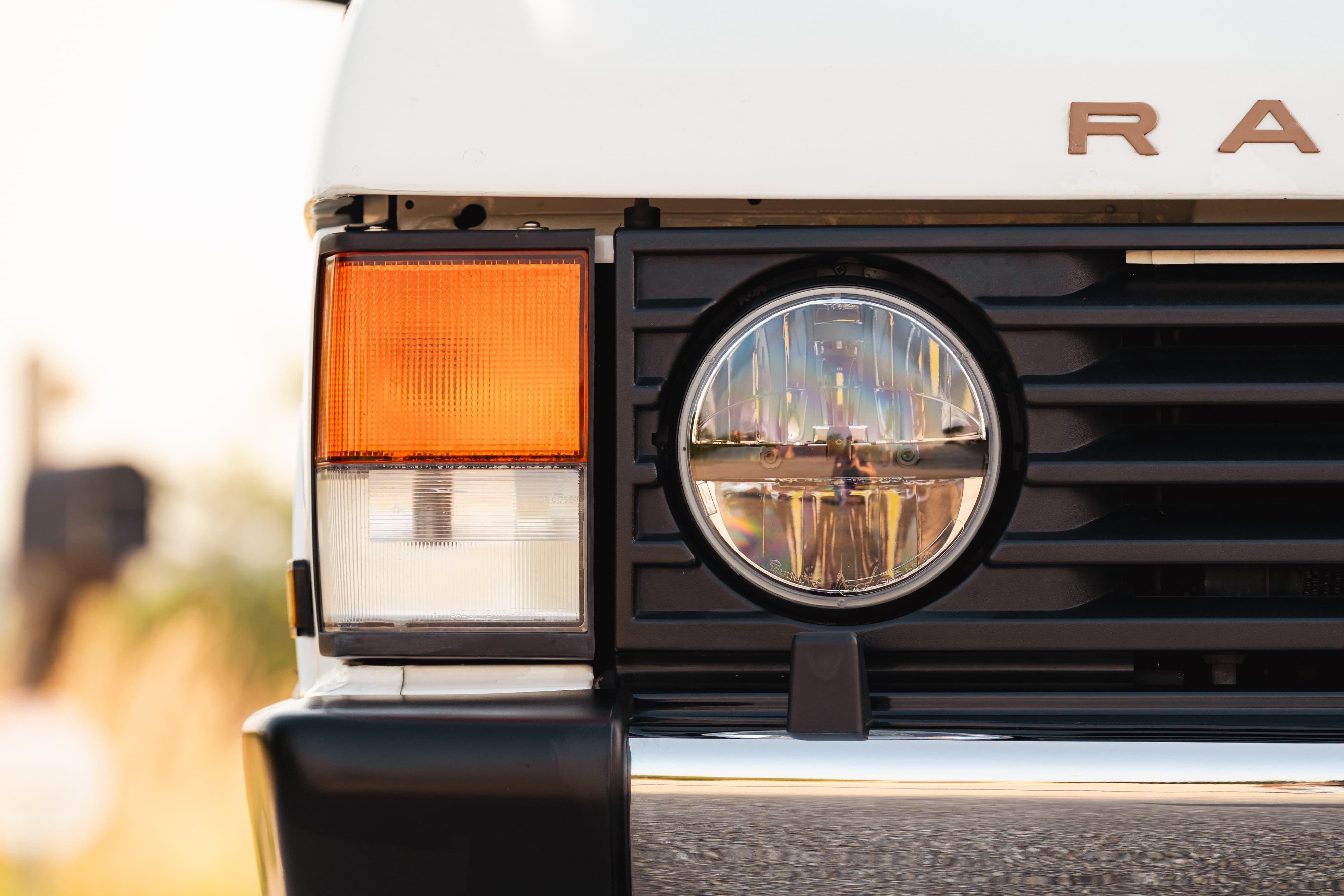 Close-up of a white 1995 Range Rover County's front grille, amber turn signal, and round headlight.