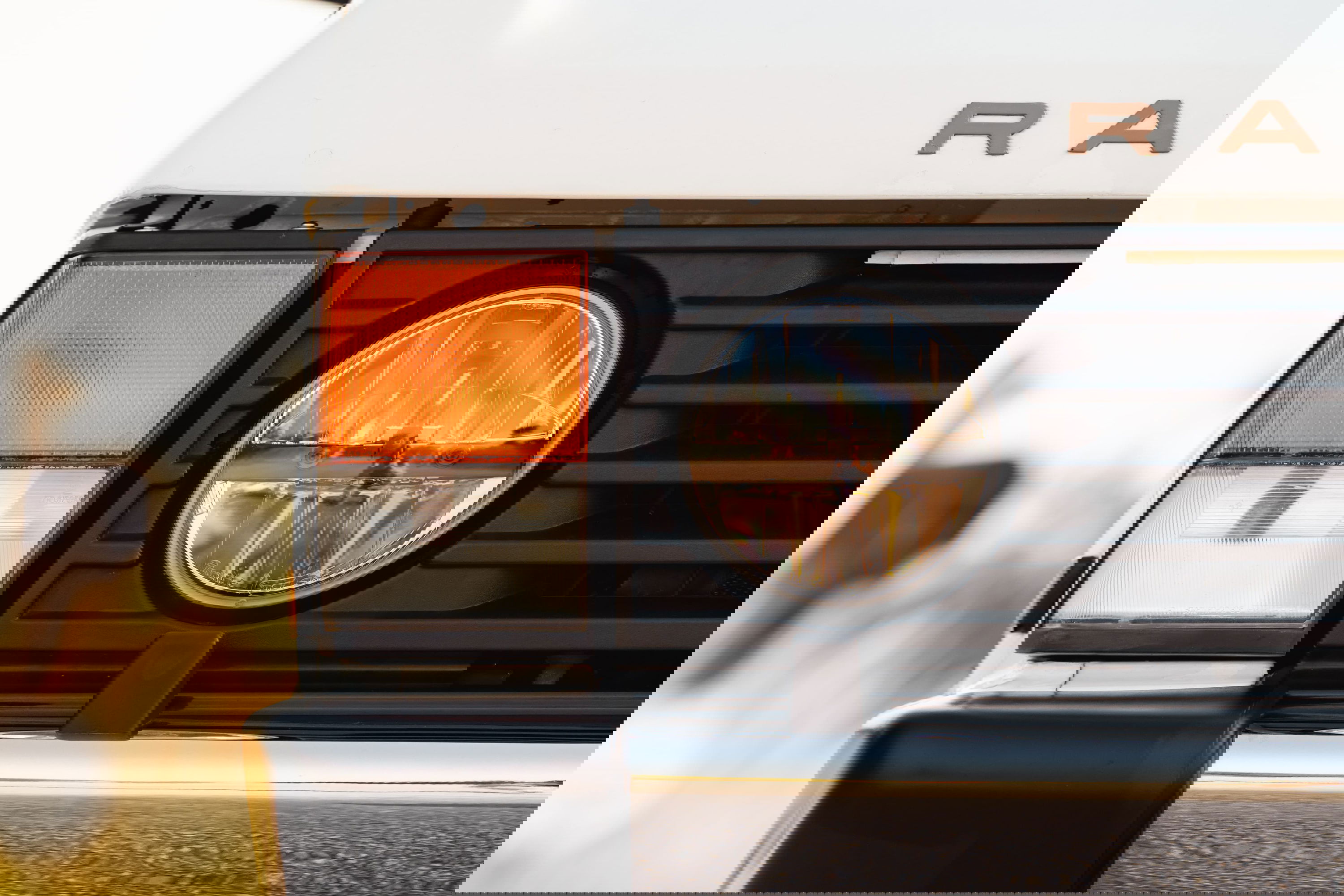 Close-up of a white 1995 Range Rover County's front grille, amber turn signal, and round headlight.