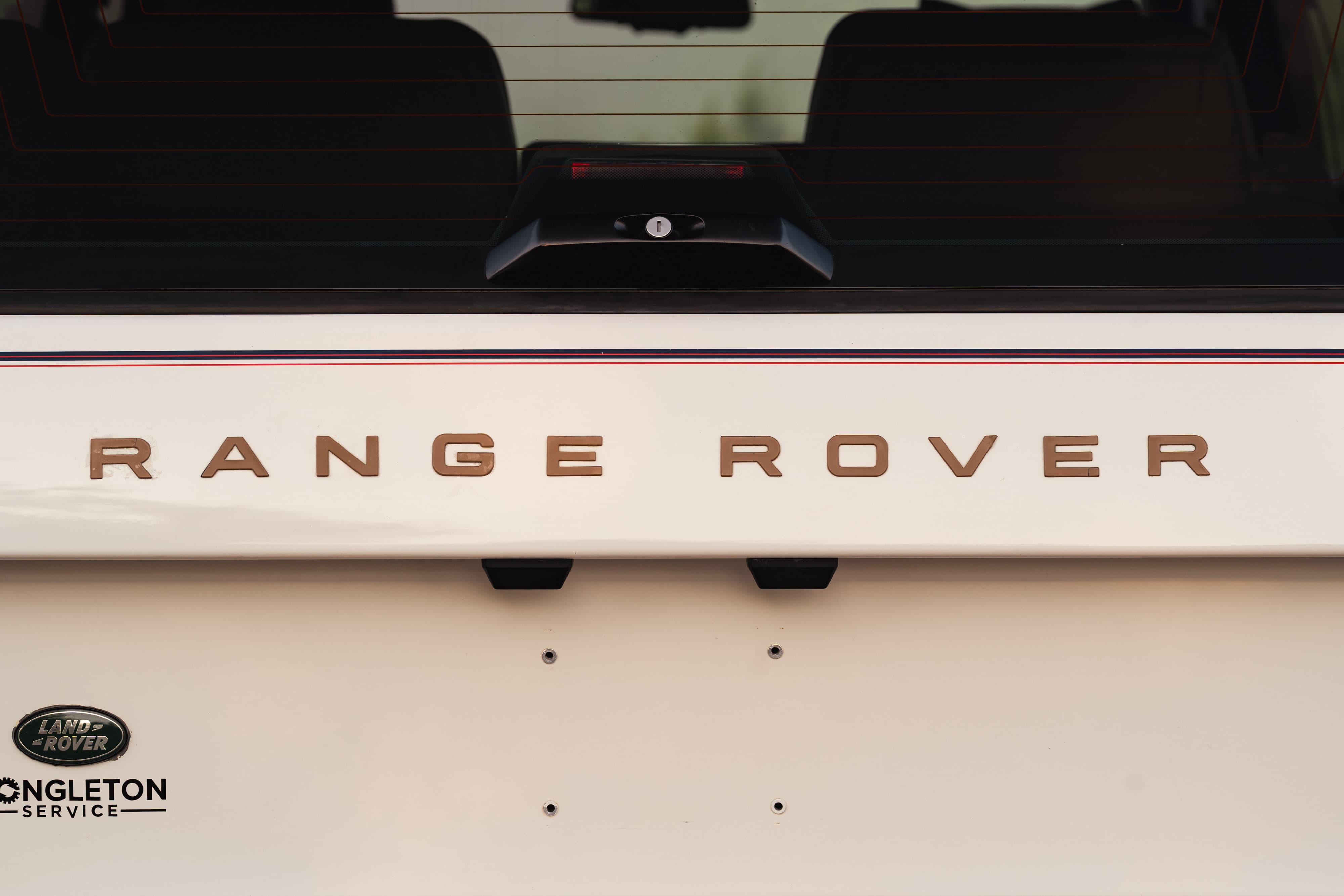 Close-up of a white 1995 Range Rover County tailgate with bronze &quot;RANGE ROVER&quot; badging.
