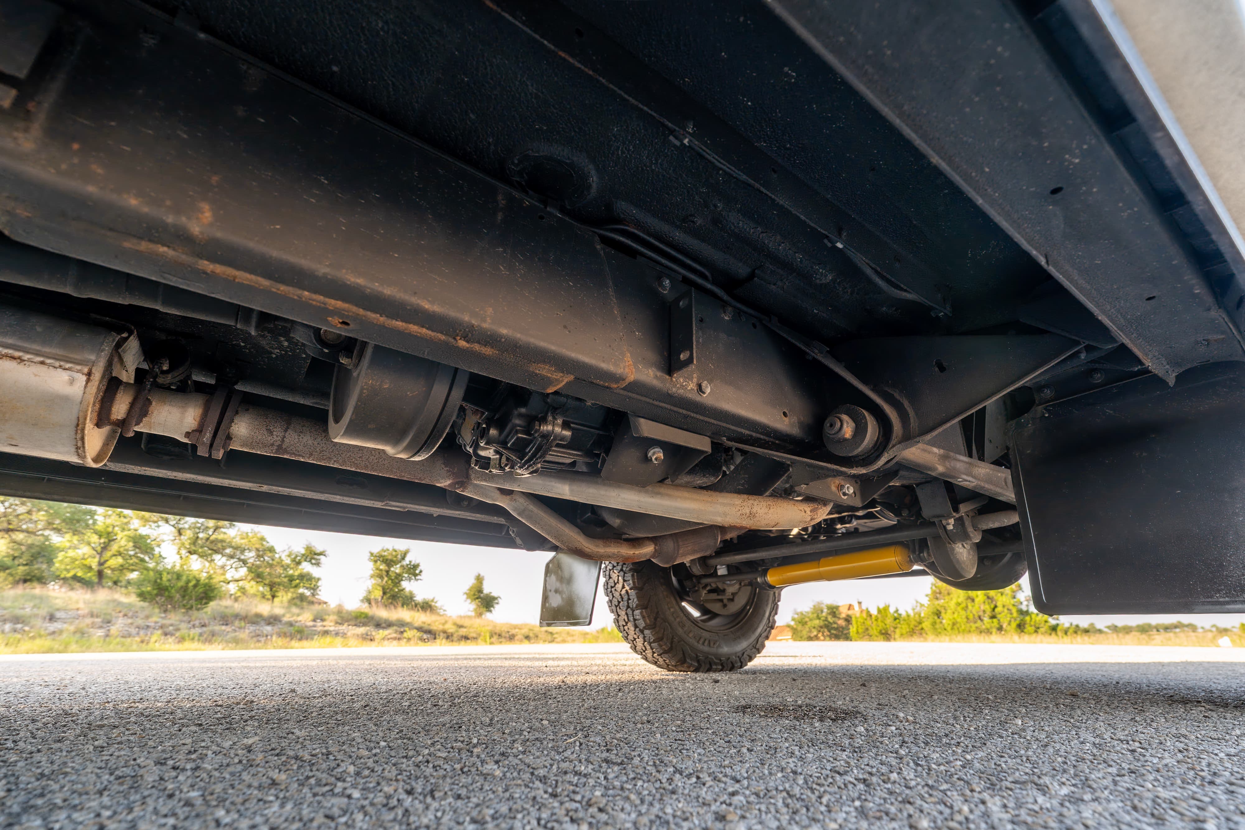 Undercarriage view of a white 1995 Land Rover Range Rover County with yellow shock absorbers and mud flaps.