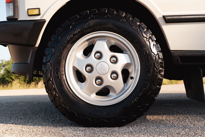 Close-up of a white 1995 Land Rover Range Rover County's silver 5-spoke rim and all-terrain tire.