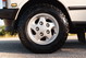 Close-up of a white 1995 Land Rover Range Rover County's silver 5-spoke rim and all-terrain tire.