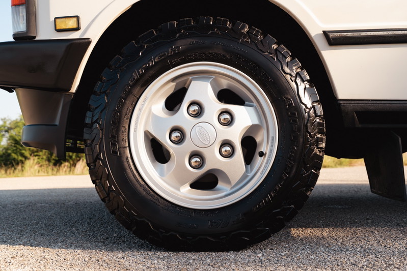 Close-up of a white 1995 Land Rover Range Rover County's silver 5-spoke rim and all-terrain tire.