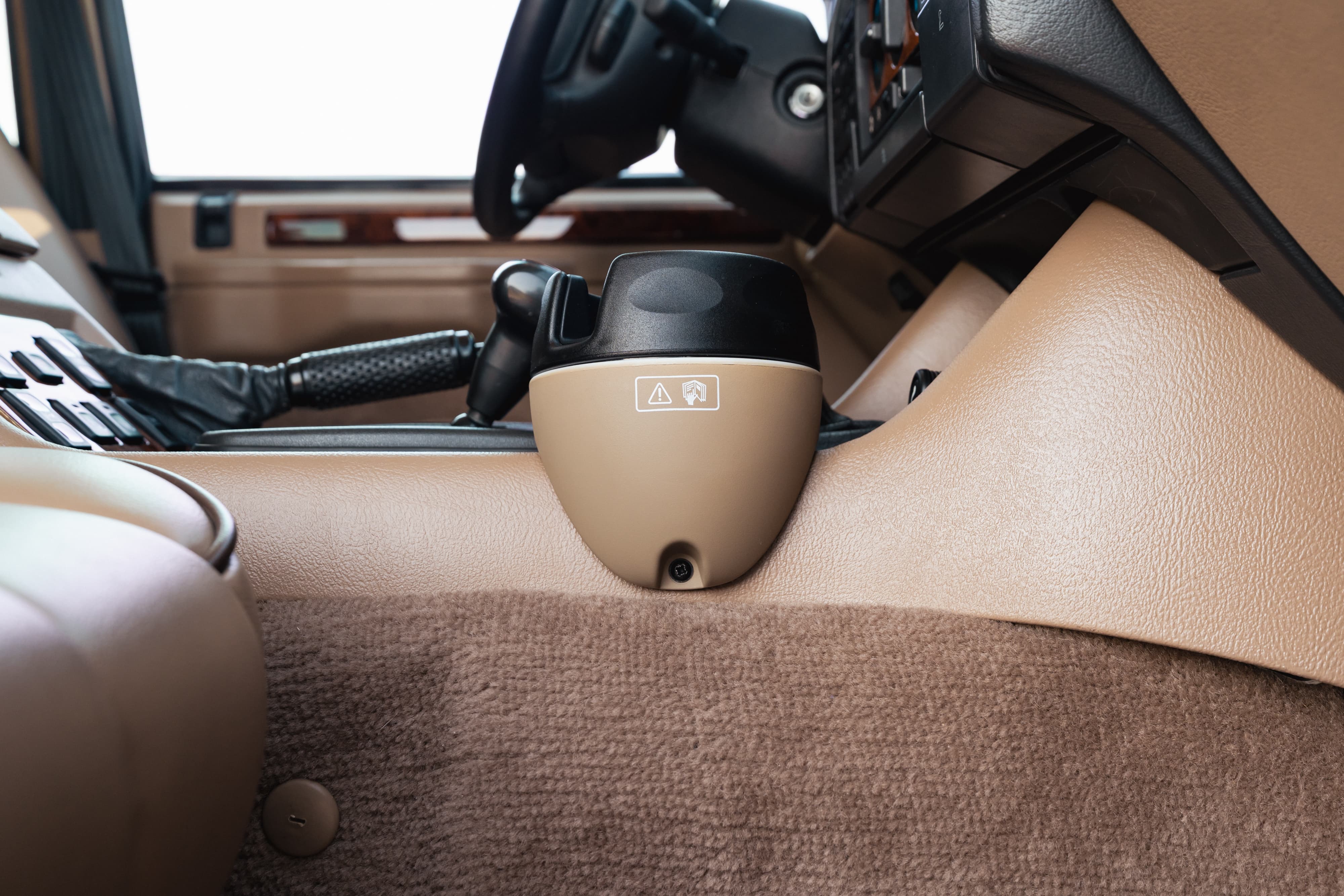 Interior of a white 1995 Land Rover Range Rover County, showing the tan dashboard, floor mats, and center console with cup holder.