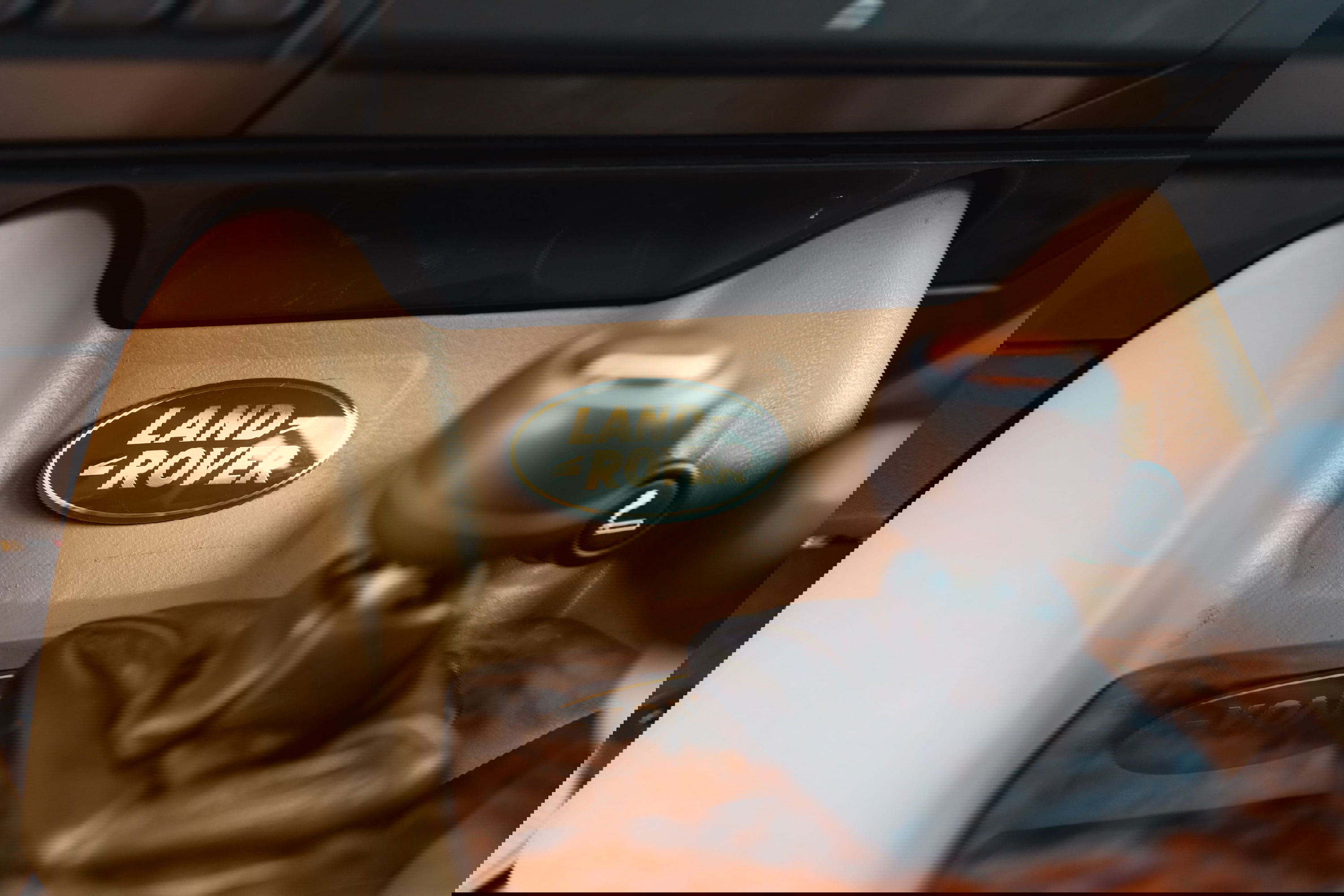 Close-up of the Land Rover logo badge on a tan dashboard trim, next to the gear shifter.