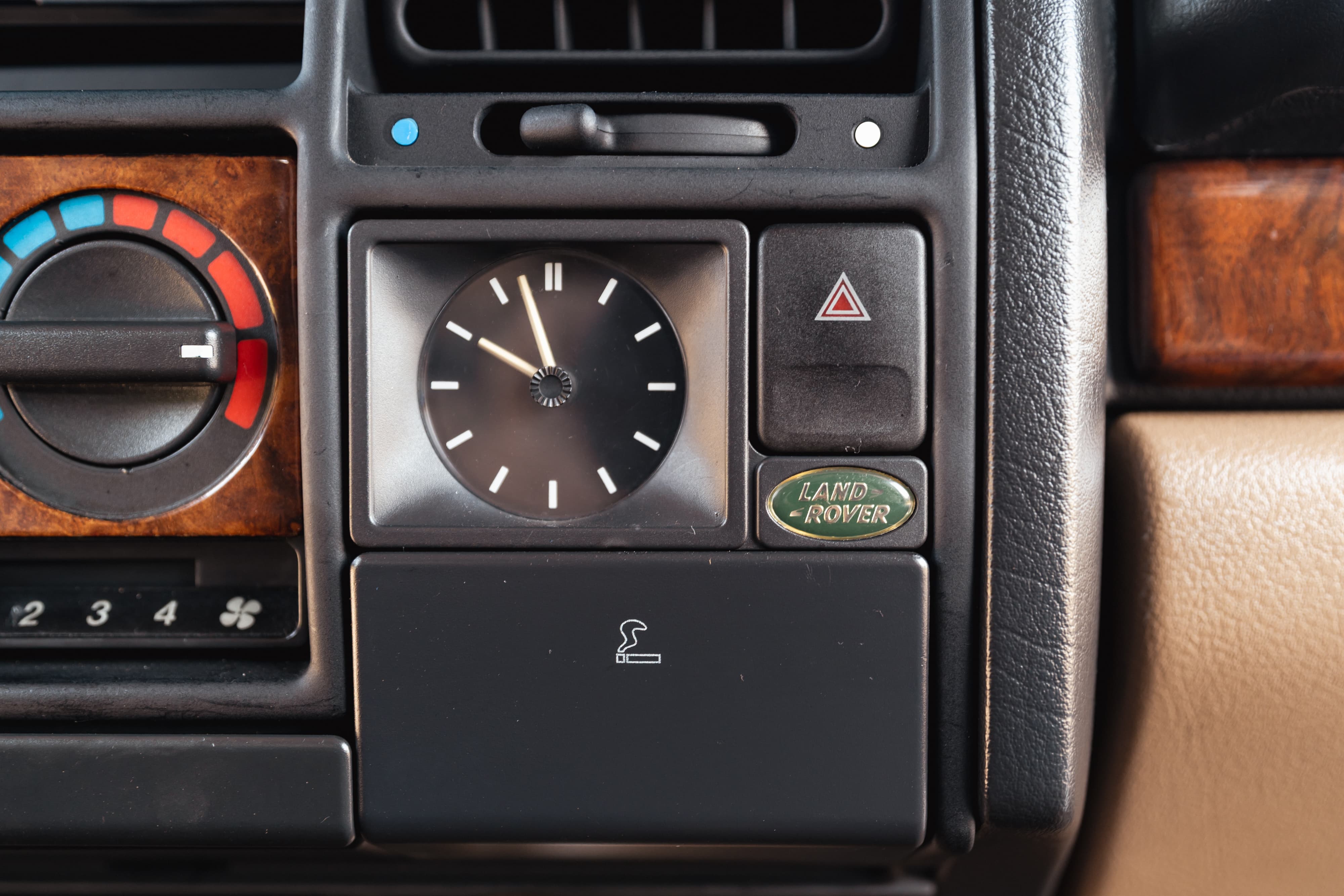Interior dash of a white 1995 Range Rover. Features climate controls, clock, hazard lights, and Land Rover badge.