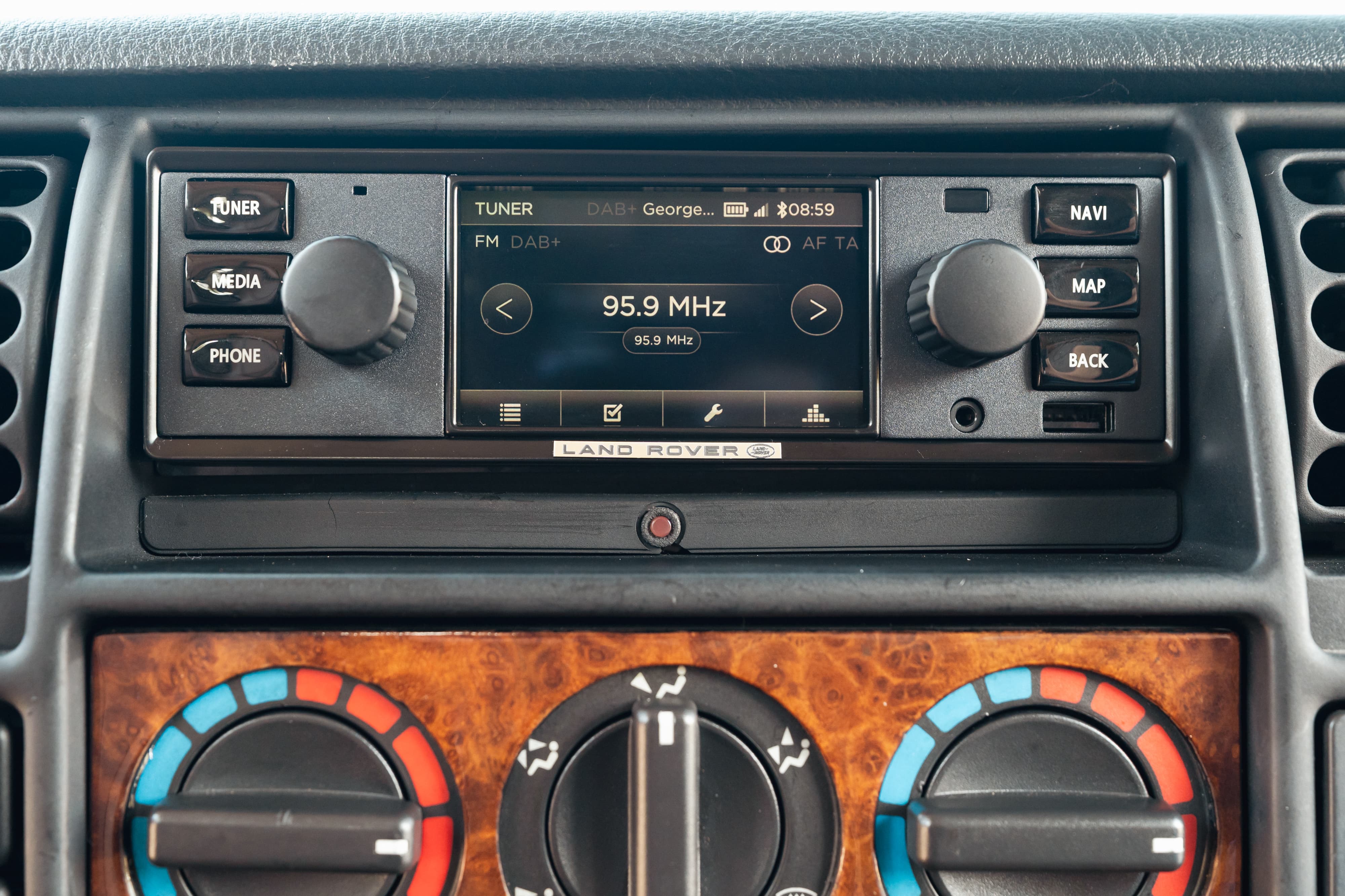 Interior of a white 1995 Land Rover Range Rover County, showing the dashboard infotainment system and climate controls.