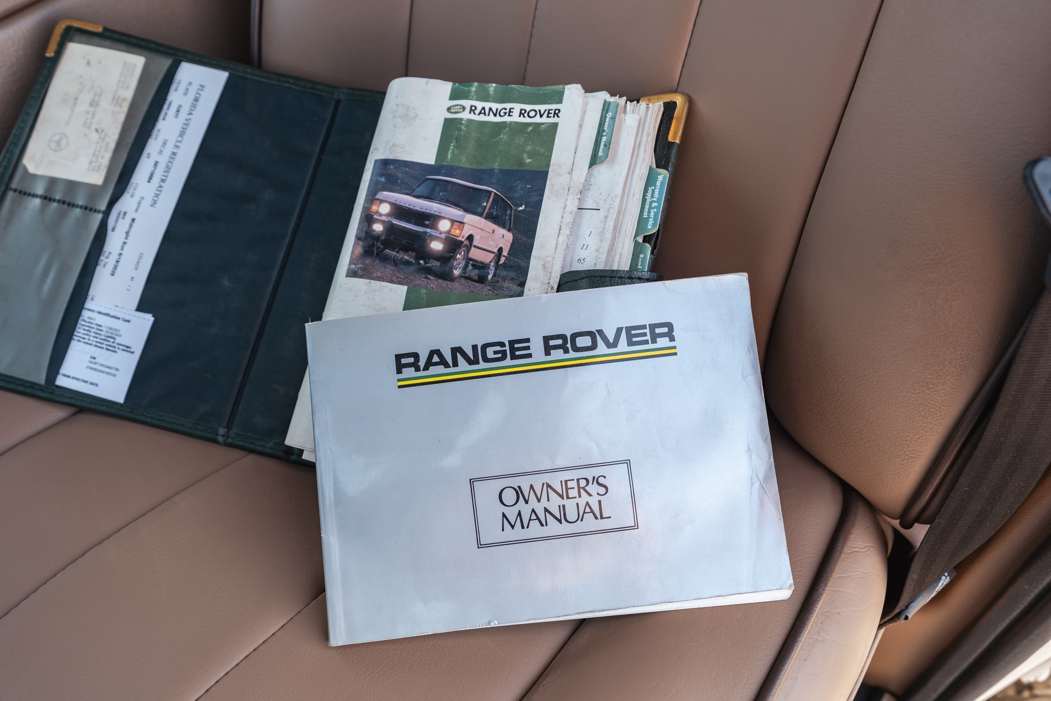 1995 white Range Rover County owner's manual and vehicle documentation open in tan leather seat.