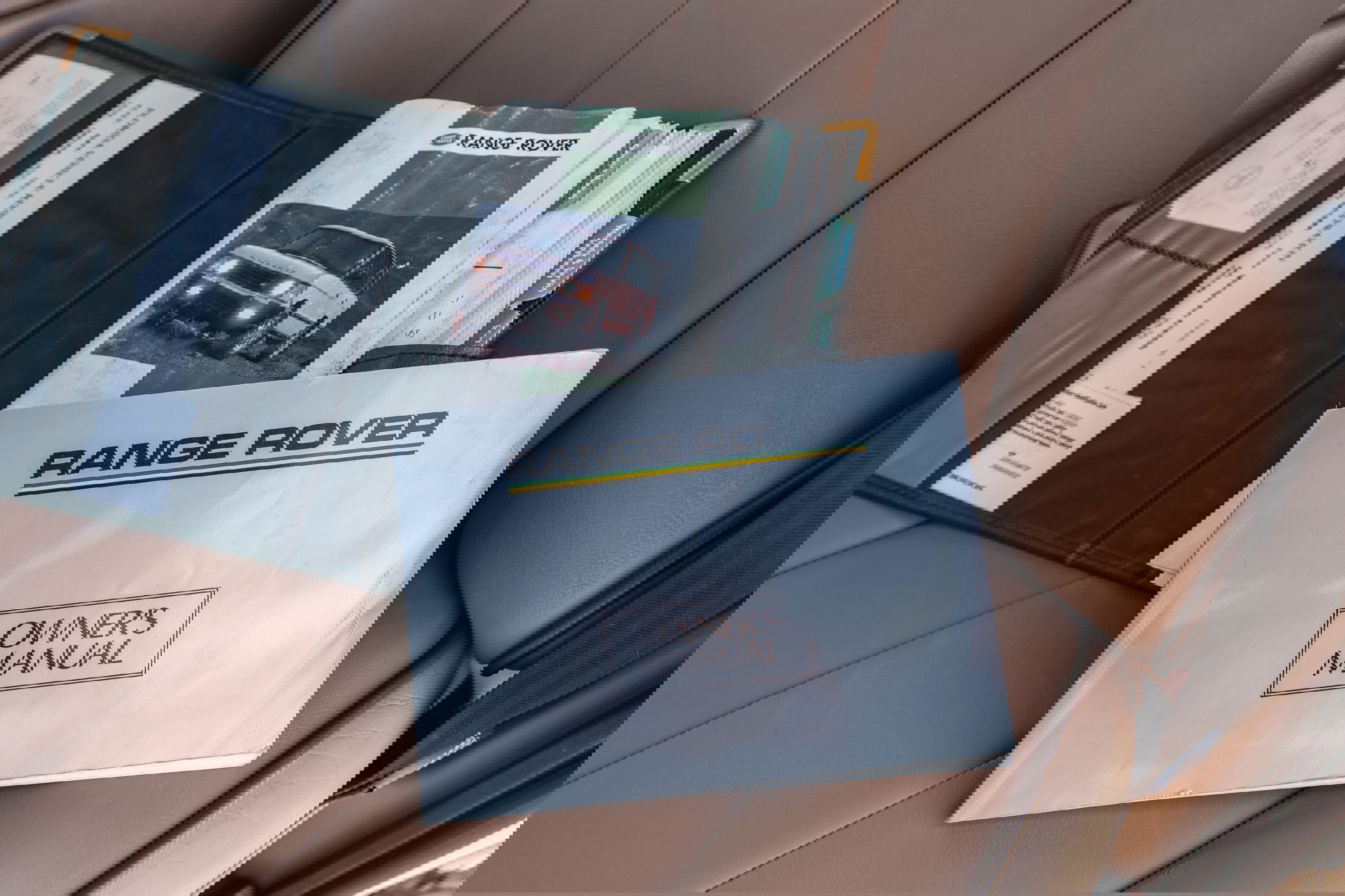 1995 white Range Rover County owner's manual and vehicle documentation open in tan leather seat.