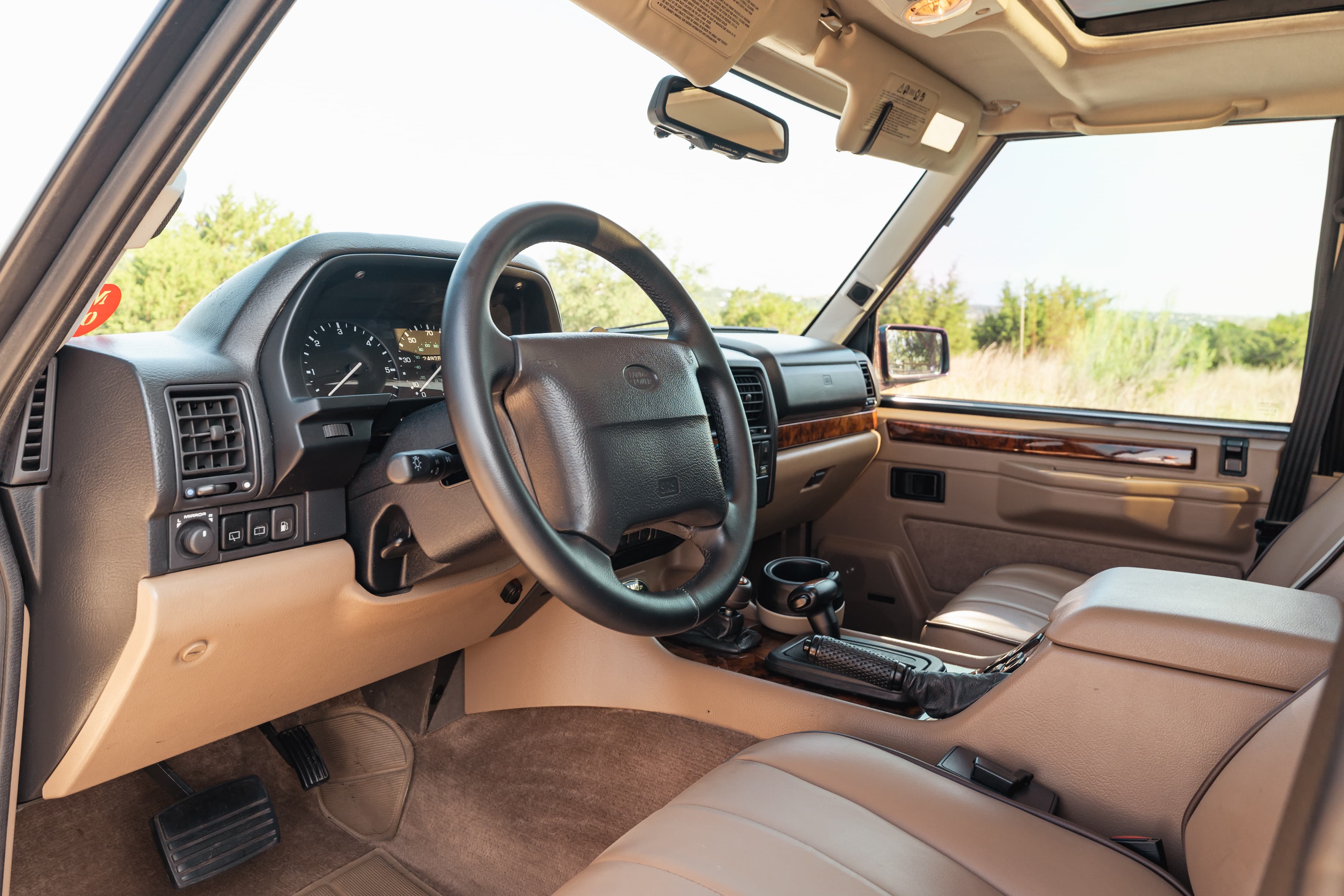 Interior of a white 1995 Land Rover Range Rover County, showing the dashboard, steering wheel, and tan leather seats.