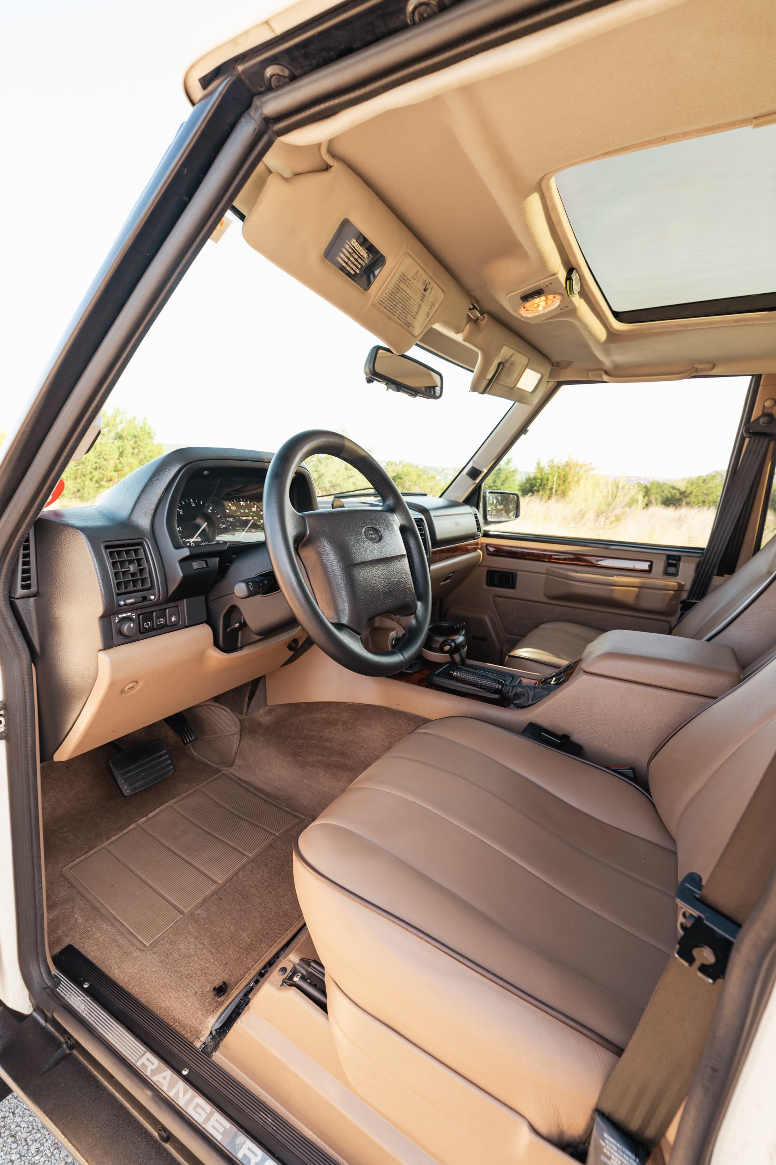 Interior of a white 1995 Land Rover Range Rover County. Tan leather seats, wood trim, sunroof.