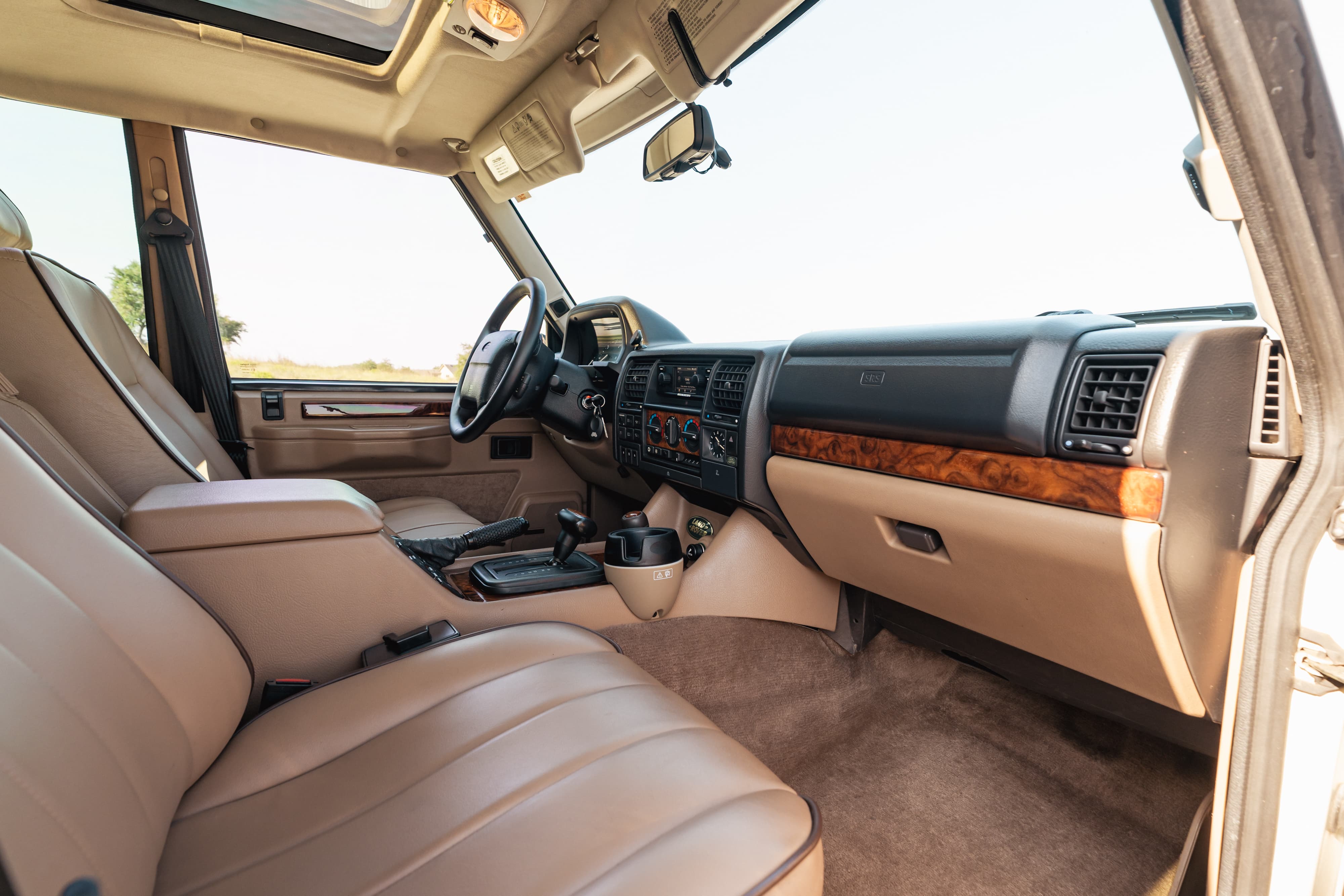 Interior view of a white 1995 Range Rover County, showcasing tan leather seats and wood trim.