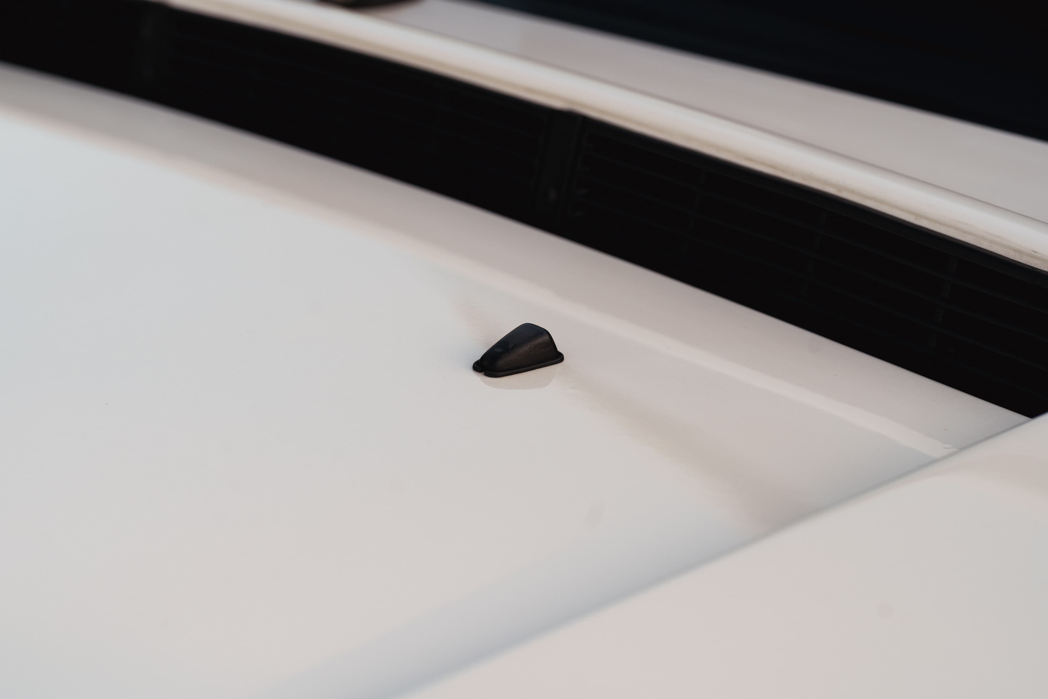 Black windshield washer nozzle on the hood of a white 1995 Land Rover Range Rover County.