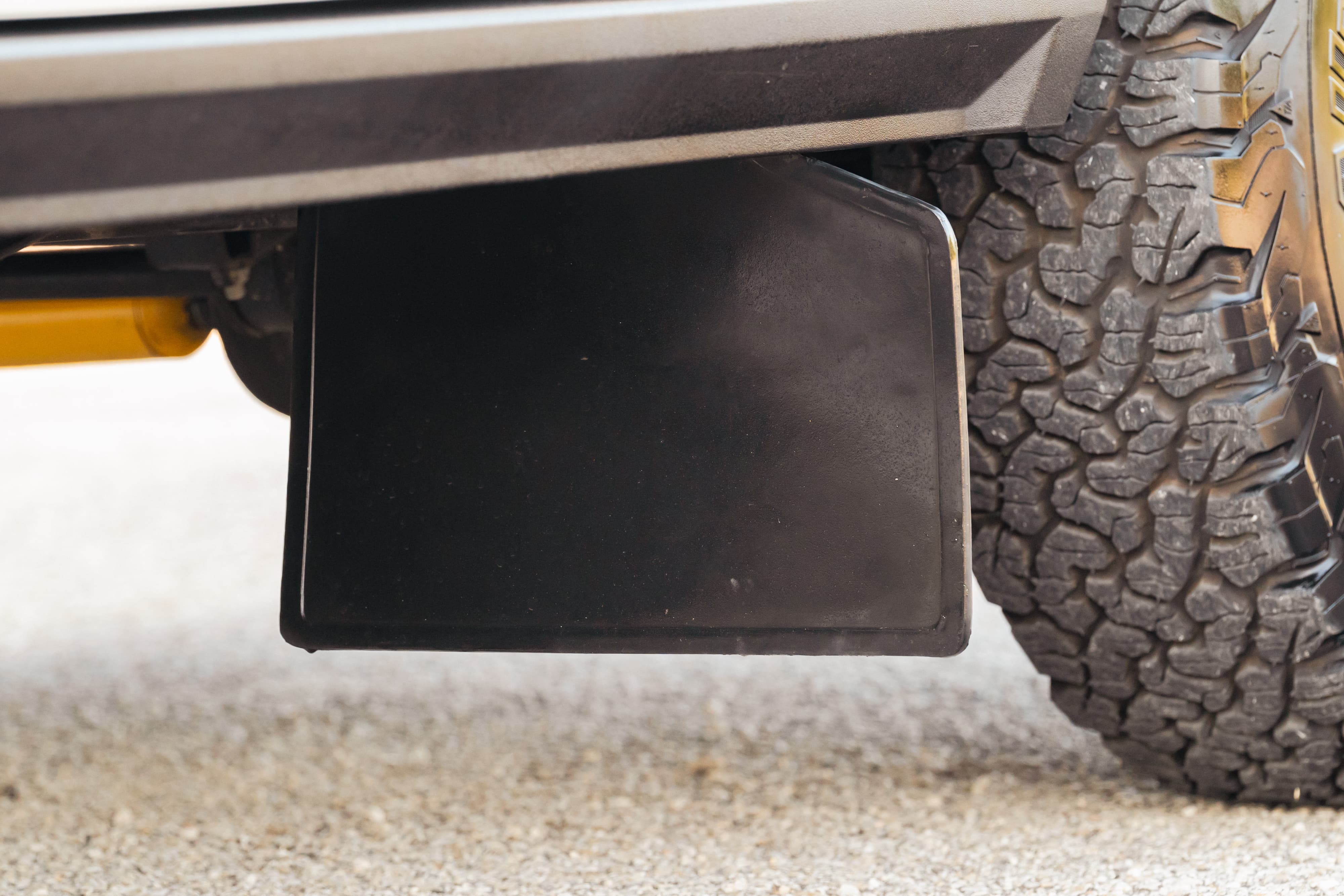 Close-up of a black mud flap and off-road tire on a white 1995 Land Rover Range Rover County.