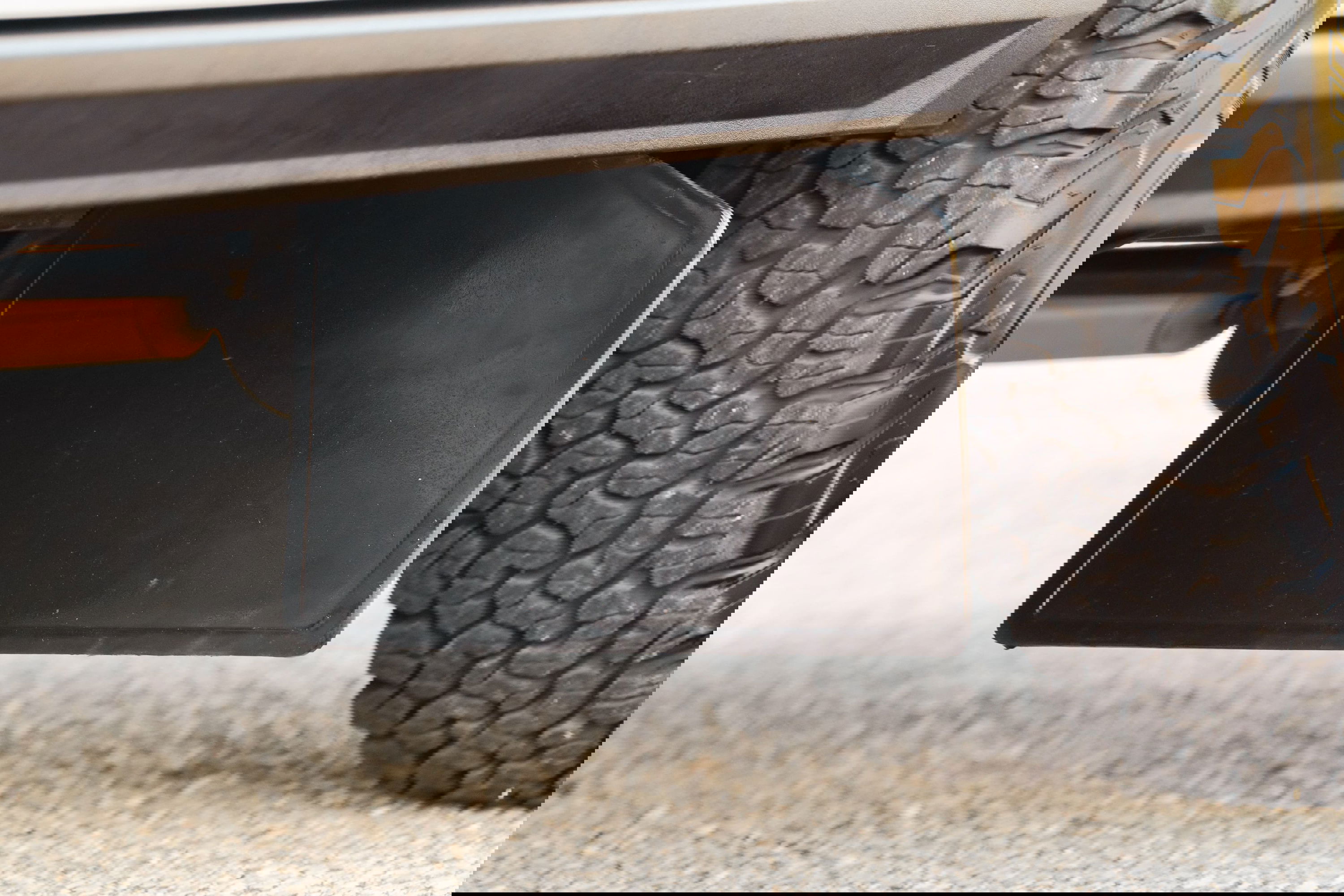 Close-up of a black mud flap and off-road tire on a white 1995 Land Rover Range Rover County.