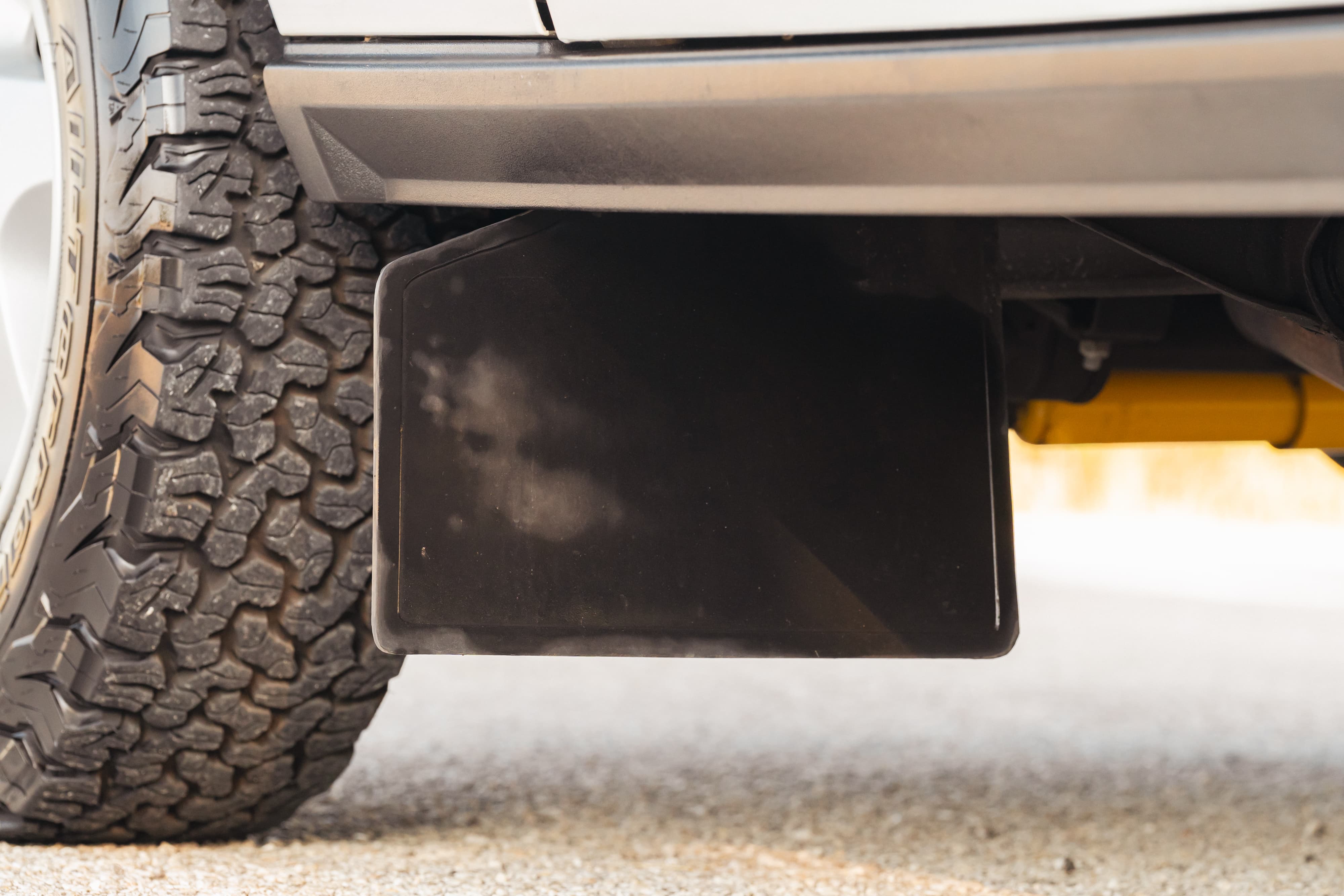 Close-up of a black mud flap and off-road tire on a white 1995 Land Rover Range Rover County.
