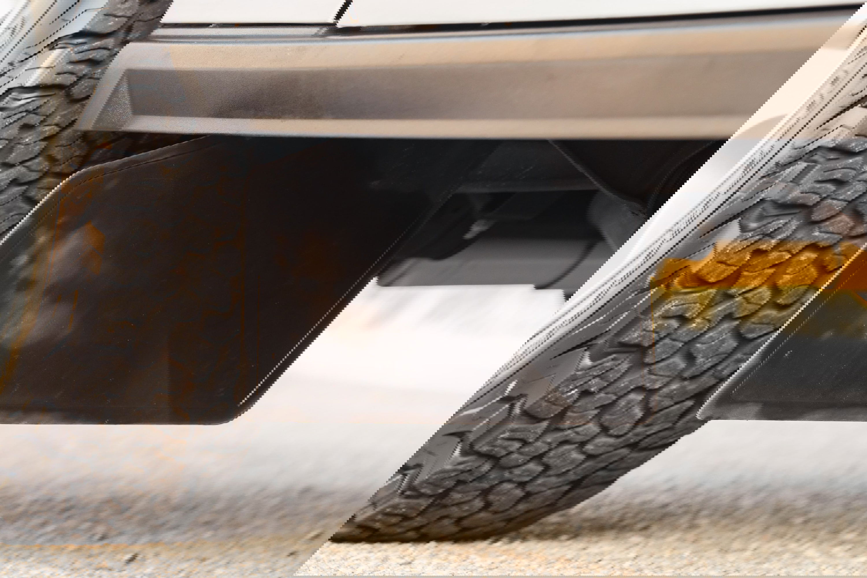 Close-up of a black mud flap and off-road tire on a white 1995 Land Rover Range Rover County.